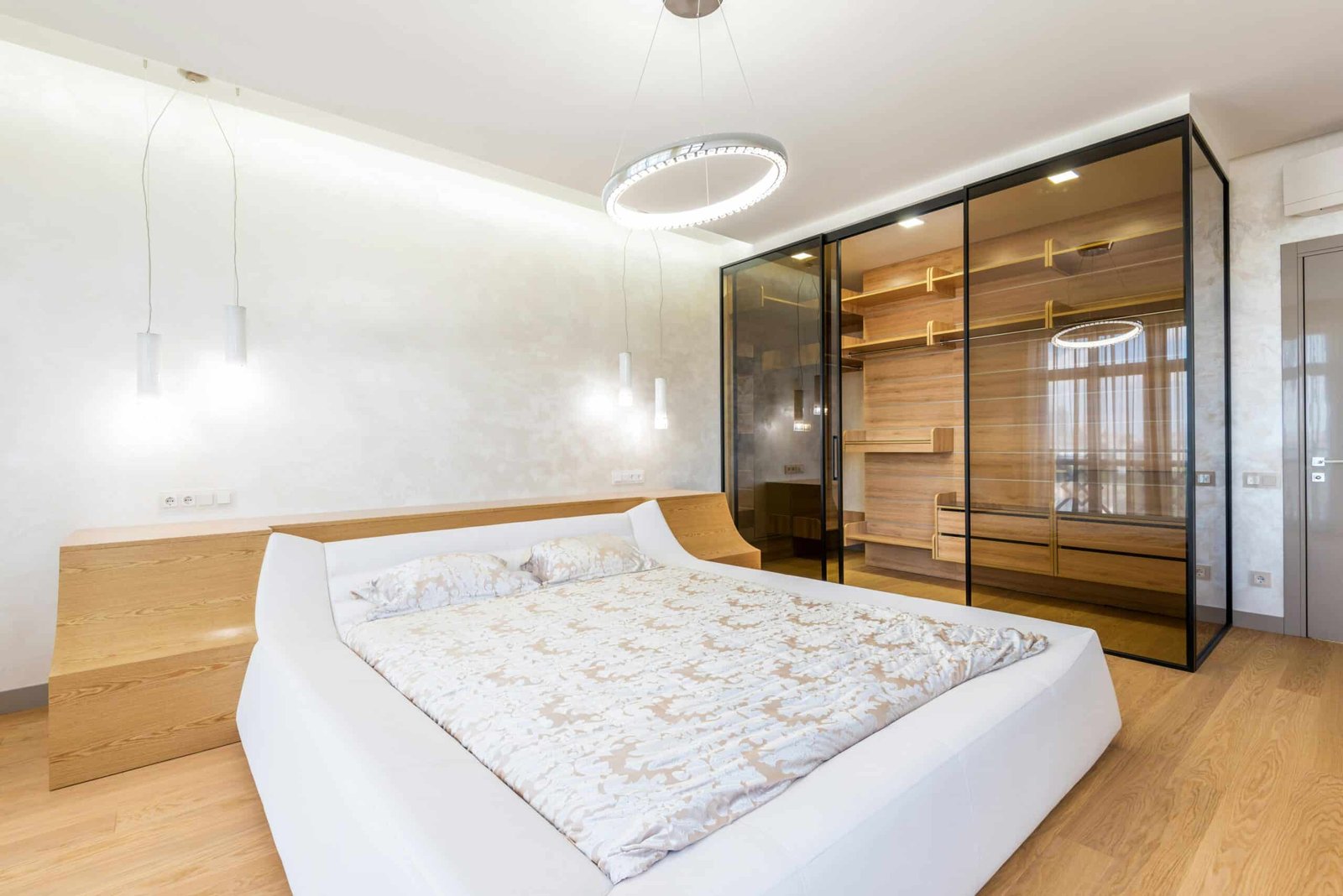 Elegant modern bedroom with a luxurious bed and glass wardrobe in a bright interior.